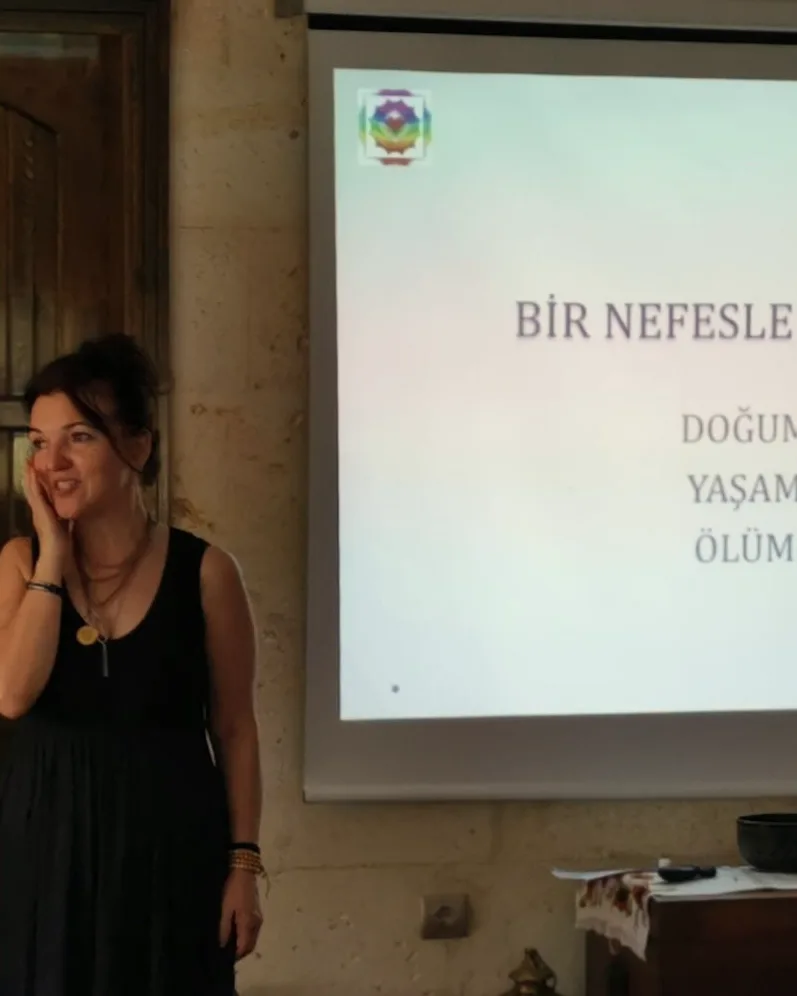 A smiling teacher in front of a slide that reads “It began with a breath: birth, life, death”